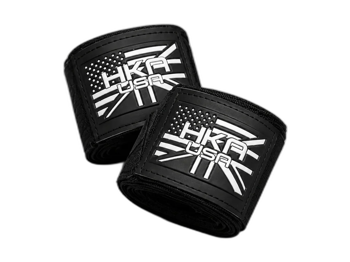 Pair of rolled black HKA USA hand wraps with white logo patches.