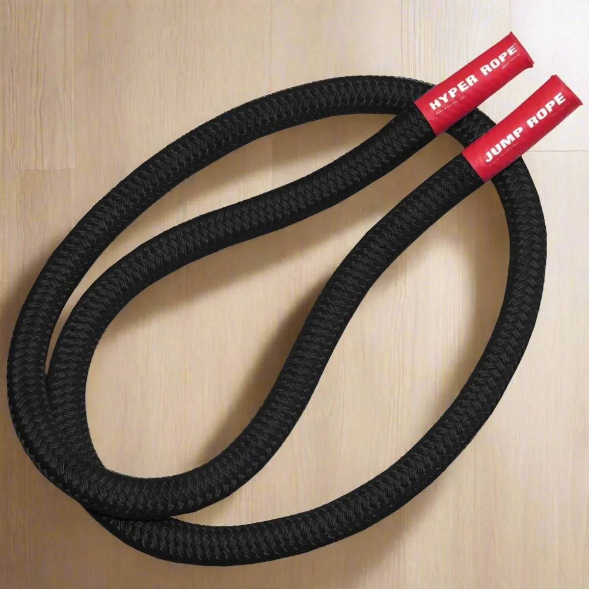 Black braided Hyperwear weighted jump rope coiled on a light wood background, with red branded end sleeves.